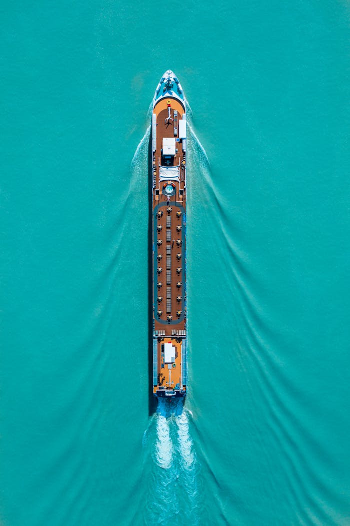 Drone shot of a cruise ship navigating turquoise waters, creating ripples and waves.